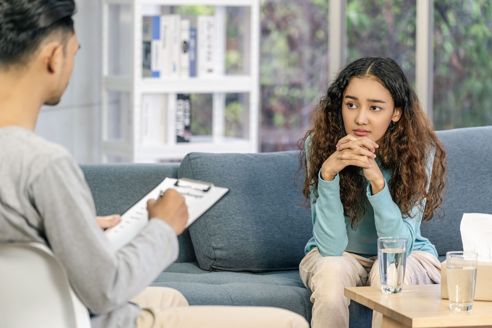 Rear view of coach listening and looking Asian young woman is sadness about their problem, Psychologist couple and hypnosis deny and argue,life coach and coaching in private indoor home concept